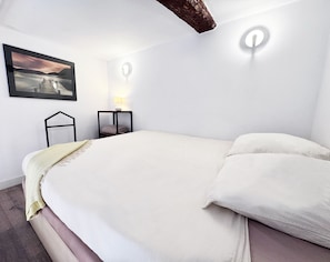 Ein Schlafzimmer mit einem Bett, einem Nachttisch, einer Lampe, einer Wandleuchte und einem gerahmten Bild.