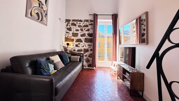 Ein Wohnzimmer mit Steinwand, einer schwarzen Ledersofa, einem Holz-TV-Schrank und einer Treppe.