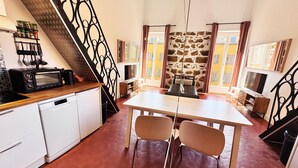 Eine kleine Küche mit Mikrowelle, Toaster und Schränken, ein Essbereich mit Tisch und Stühlen sowie eine Treppe mit dekorativer Geländer.