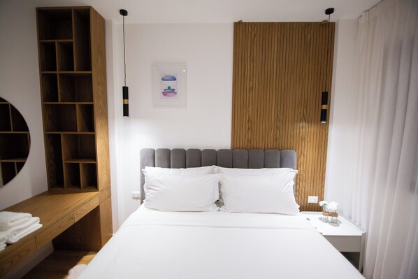 Une chambre à coucher comprenant un lit, une étagère en bois, une tête de lit, une table de chevet et un luminaire fixé au mur.
