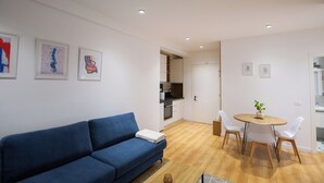 A modern living room with a blue sofa, a dining table with chairs, and a kitchen area in the background.