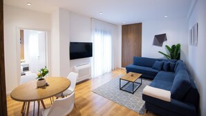 A modern living room with a sofa, a coffee table, a TV, and a dining area with chairs and a table.