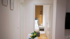 A hotel hallway with a wooden floor, a white wall, and a bed in the background.