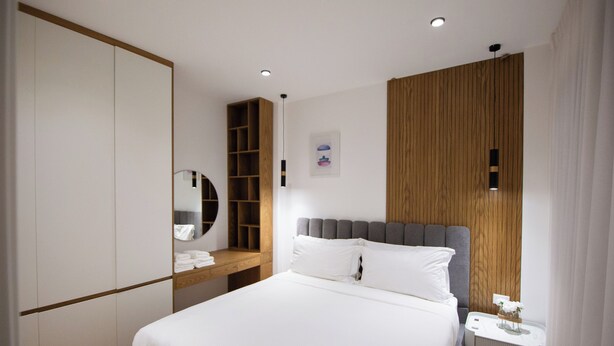 A modern bedroom with a large bed, a wardrobe, a bedside table, and a wooden panel wall.