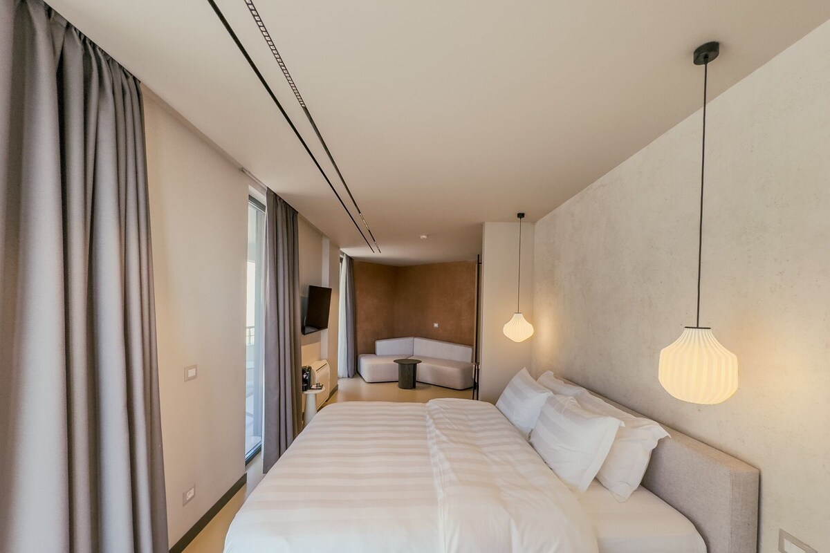 A hotel room with a large bed, a sofa, a TV, and a coffee machine.