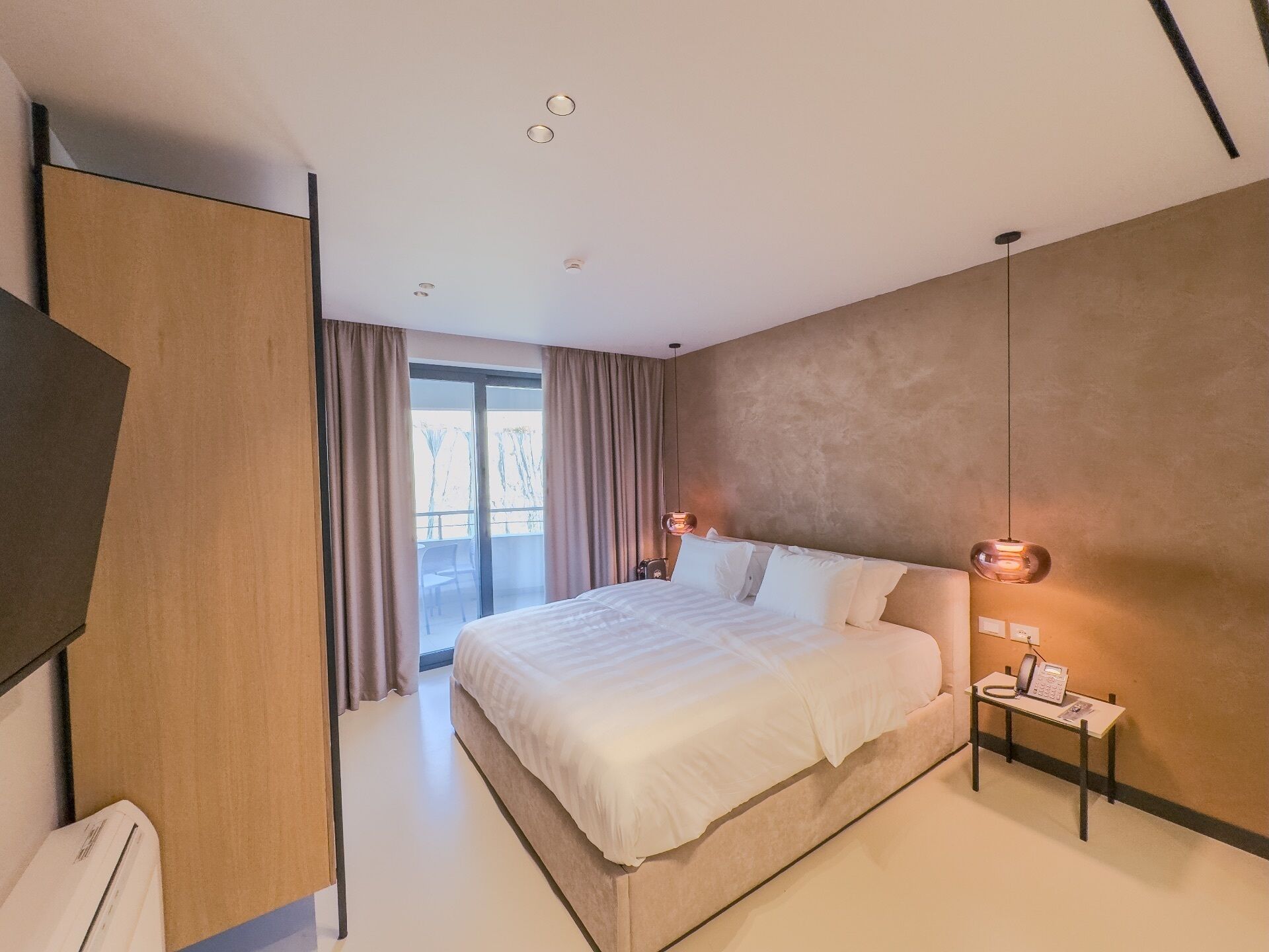 A modern hotel room with a large bed, a desk with a telephone, and a view of the outdoors.