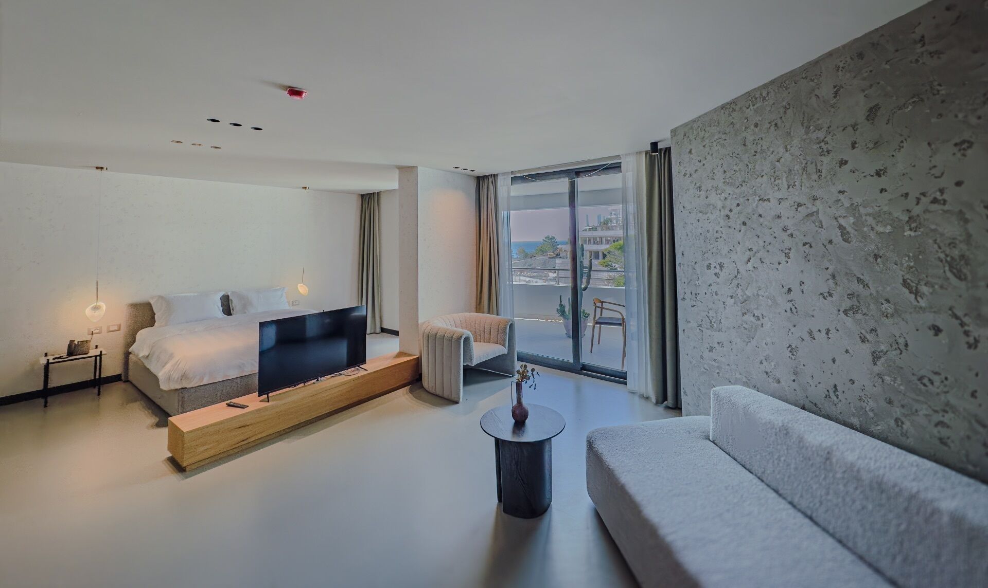 Une chambre d’hôtel moderne, équipée d’un lit, d’un canapé, d’une petite table et offrant une vue sur l’extérieur.