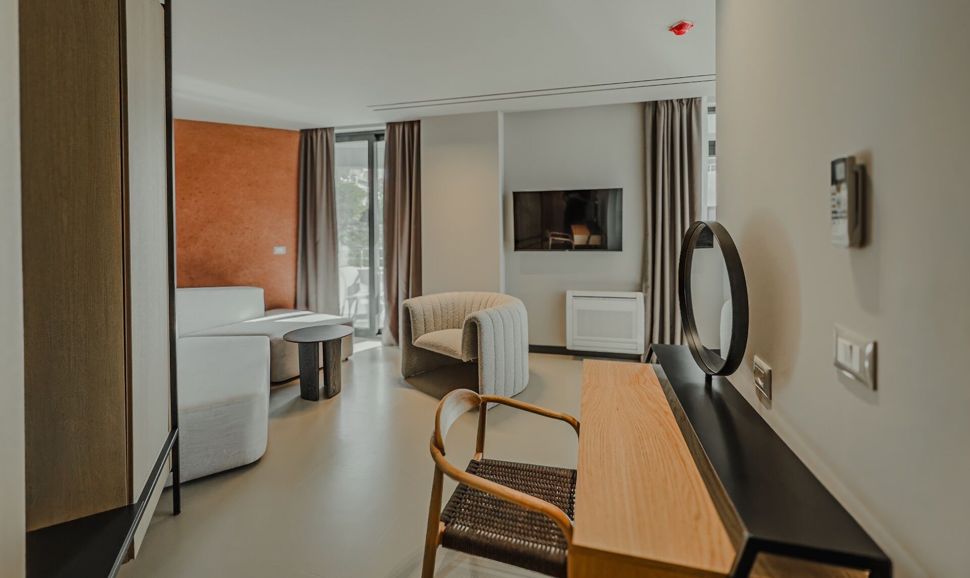 A hotel room with a sofa, a chair, a small table, a TV, and a mirror.