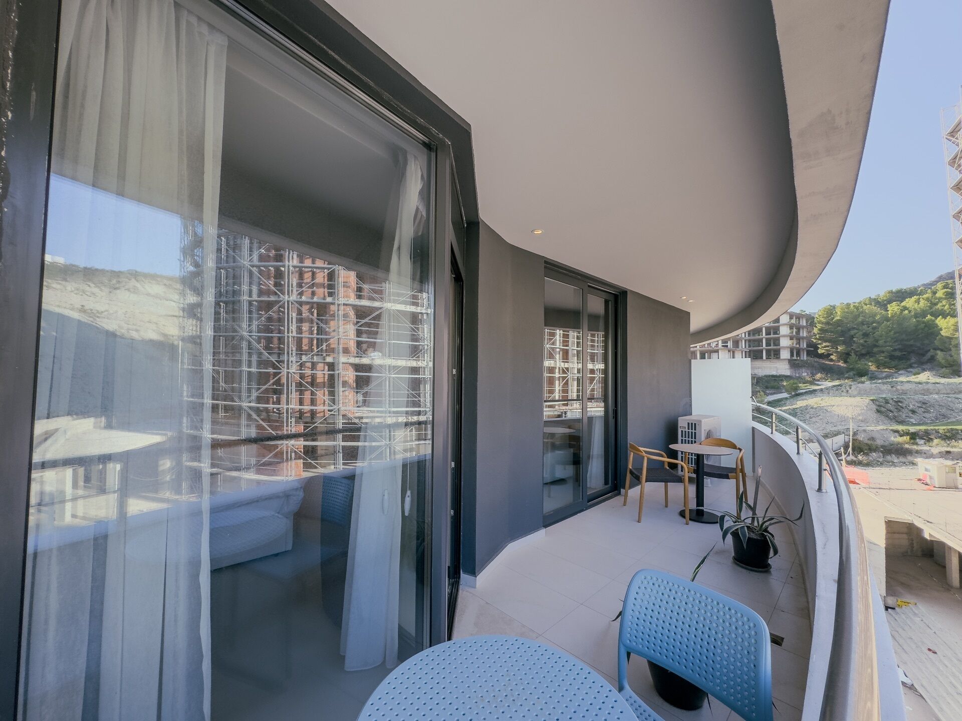 Un balcon avec une table et des chaises, un pot de fleurs et une vue sur un immeuble en construction.