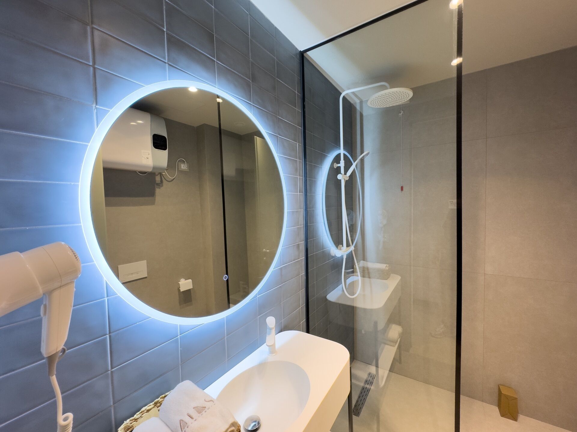 Une salle de bain moderne avec un miroir rond, une douche à parois de verre et un lavabo blanc.
