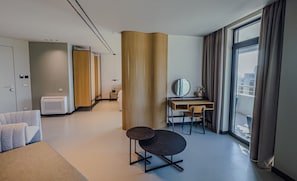Habitación de hotel con cama, escritorio, silla, espejo y un amplio ventanal con cortinas.