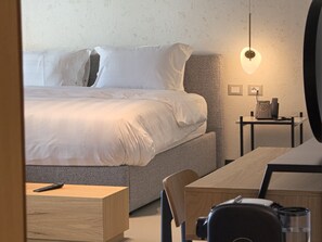 A hotel room with a bed, bedside table, lamp, and a desk with a chair. - Zins Luxury Rooms (Durrës)