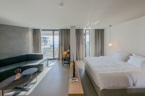 A modern hotel room with a bed, a sofa, a desk, and a view of the outdoors. - Zins Luxury Rooms (Durrës)