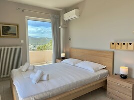 Un dormitorio con cama, mesita de noche, lámpara, equipo de aire acondicionado, ventana con cortinas, radiador y estante fijado a la pared.