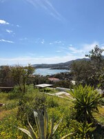 Un paisaje costero con vista al mar, vegetación y colinas distantes.