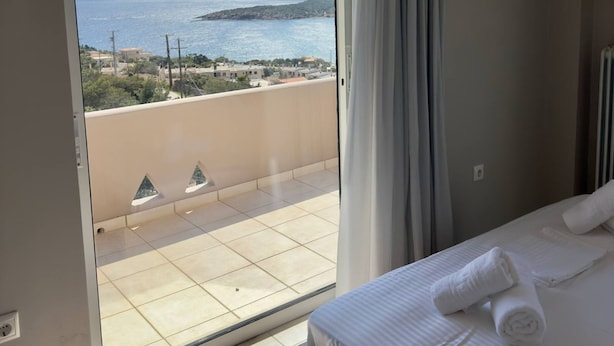 A hotel room with a large sliding glass door leading to a balcony with a view of the sea and distant hills. - Delos House Sounio Sea View Temple of Poseidon (Lavreotiki)