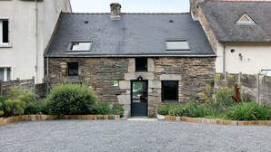 Un bâtiment en pierre avec une porte sombre, une petite fenêtre et une allée gravillonnée.