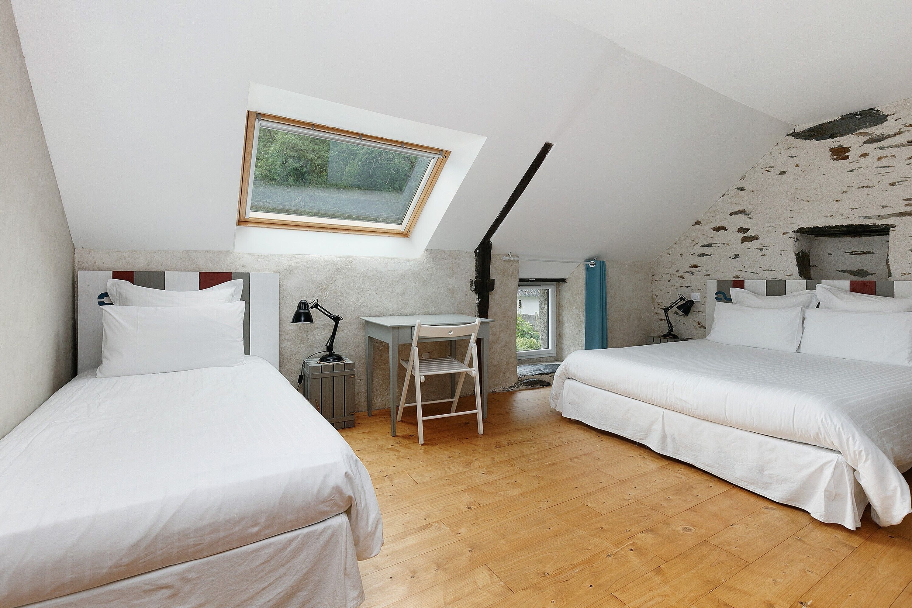 Una camera da letto con due letti, una scrivania, una sedia, un lucernario e vista sull'esterno.