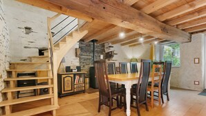 Un intérieur rustique avec un escalier en bois, une table à manger entourée de chaises et un mur en pierre.