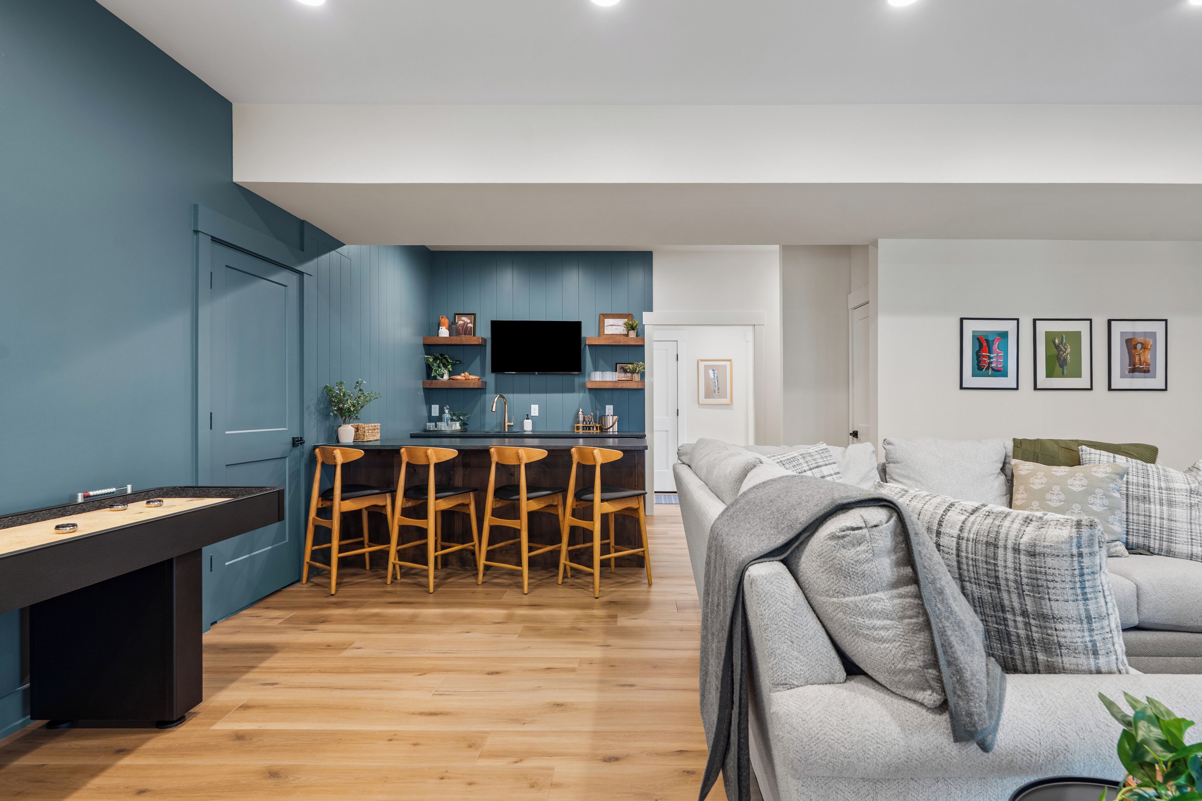 A modern living room with a pool table, a sofa, and a kitchen area with a TV and bar stools.