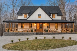 A two-story house with a covered porch, stone foundation, and a gravel driveway.