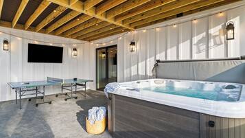 Un espacio al aire libre techado con mesa de ping pong, jacuzzi y zona de estar.