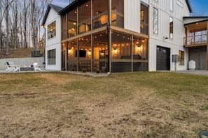 A modern two-story building with large windows, a covered outdoor seating area, and a fire pit.