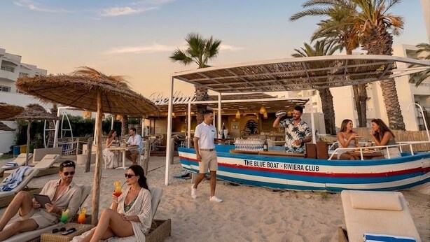 A beachside setting with lounge chairs, a bar area, and a boat named 'The Blue Boat - Riviera Club'. - Appartement S+2 vue mer & golf - Premium hotel residence in Monastir (Monastir)