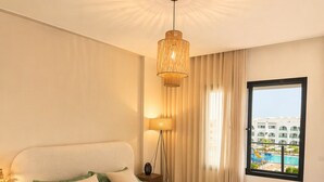 A bedroom with a bed, a nightstand, a lamp, a window with a view, and a ceiling light fixture. - Appartement S+2 vue mer & golf - Premium hotel residence in Monastir (Monastir)