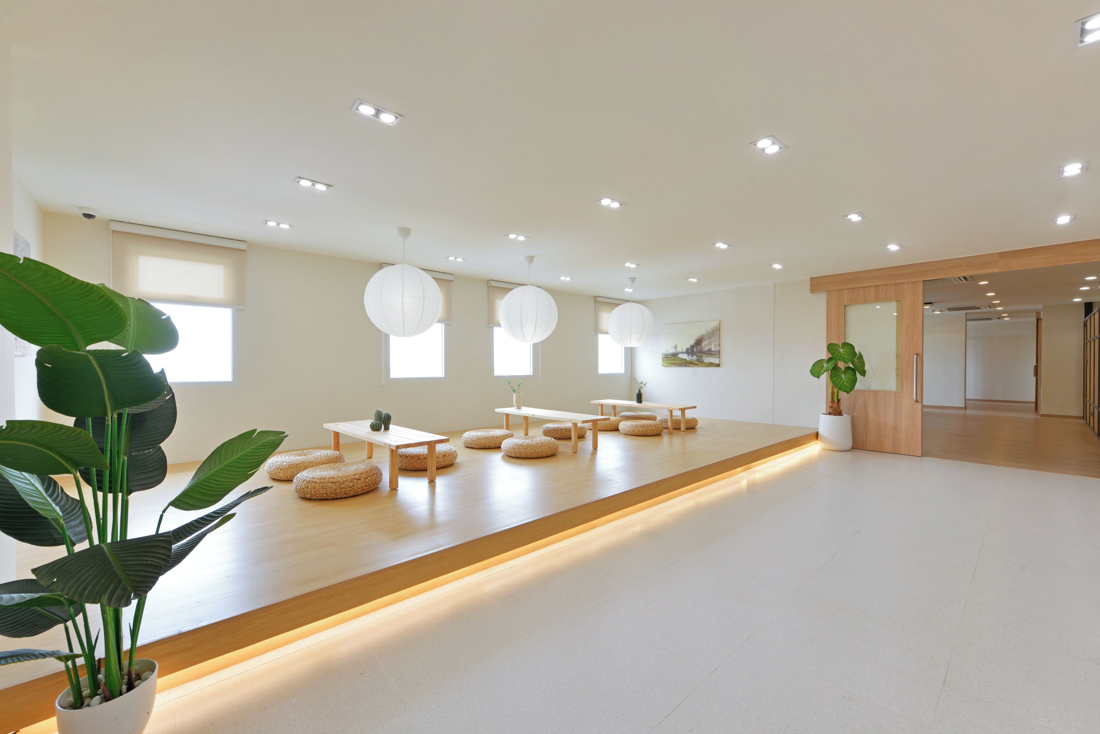 Una habitación amplia con un largo banco de madera, taburetes redondos de mimbre y una planta en maceta.