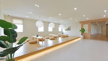 Una habitación amplia con un largo banco de madera, taburetes redondos de mimbre y una planta en maceta.