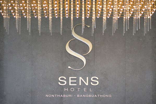 Un letrero de hotel con un logotipo grande con la letra 'S' en mayúsculas y el nombre 'SENS HOTEL' debajo, junto con la ubicación 'NONTHABURI - BANGBUATHONG'.