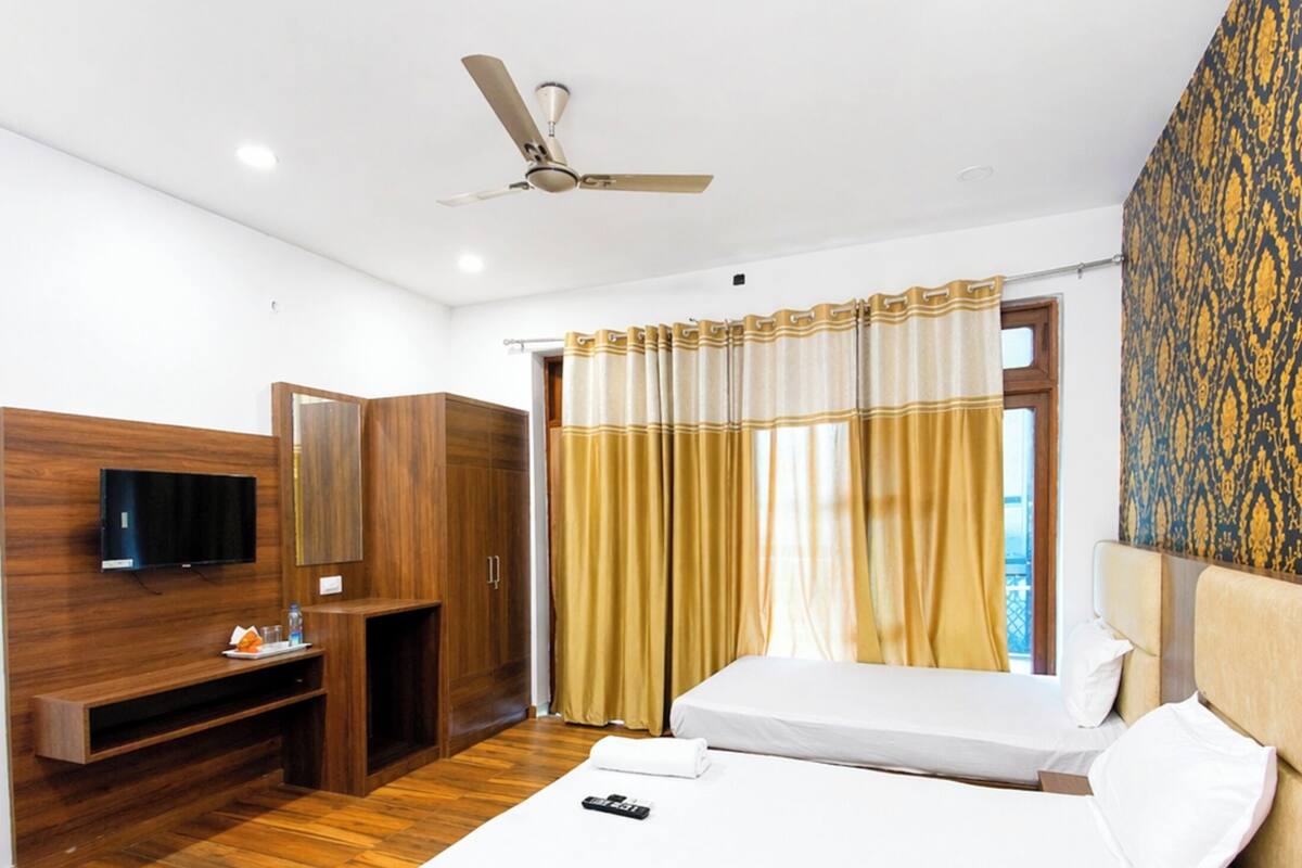 A hotel room with a bed, a TV, a desk, a wardrobe, a ceiling fan, and a window with curtains.