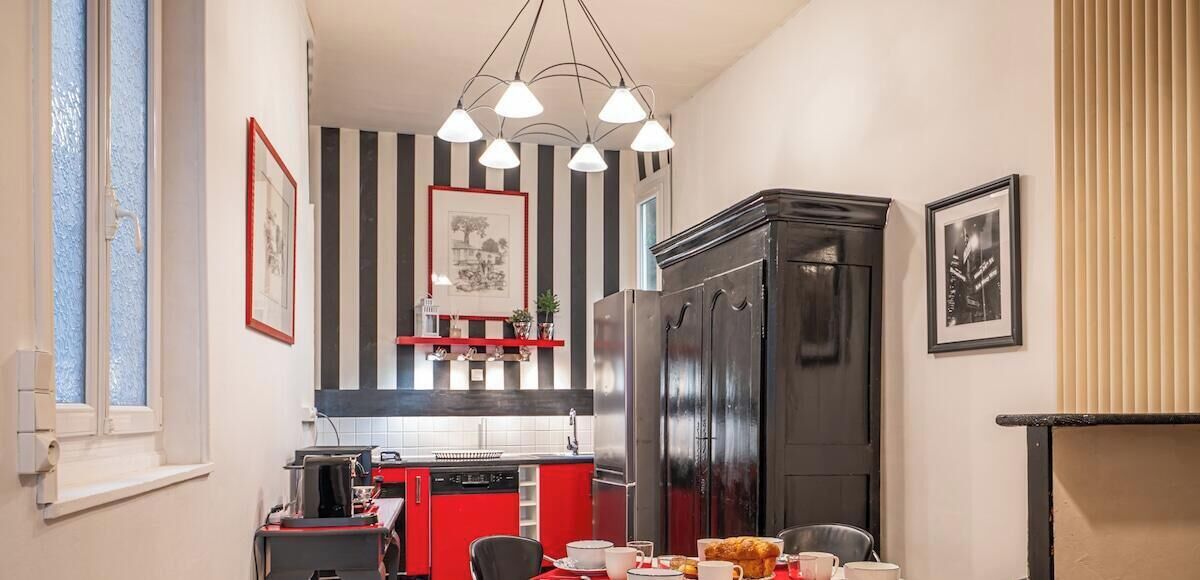 A compact kitchen with a red and black color scheme, a black refrigerator, and a dining area with a table set for two.