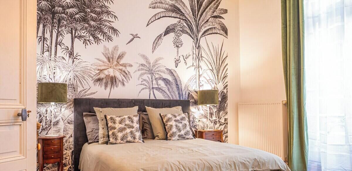 Una camera da letto con un letto, una testiera, due comodini e un muro decorato con un murale tropicale.