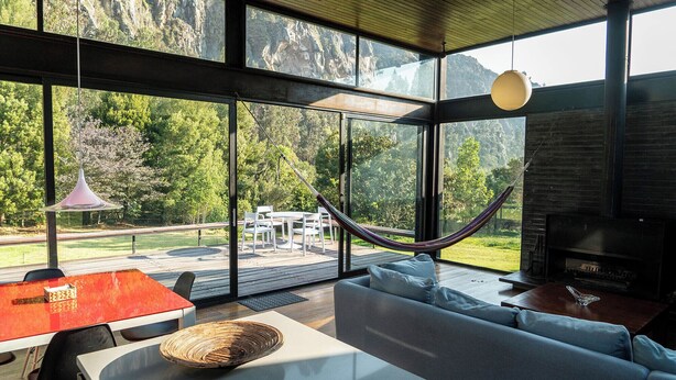 Un interior modern amb grans finestres, una cadira lliure, un sofà i una zona de menjador.