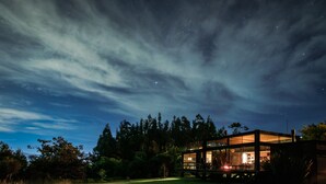 Una casa moderna amb façana de vidre, envoltada d'una zona verda i arbres, sota un cel nocturn ple d'estrelles.