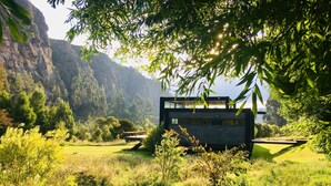 Un edifici modern amb façana de vidre, envoltat de vegetació exuberant i un paisatge de muntanyes al fons.