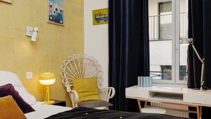 A hotel room with a bed, a chair, a desk, a window with curtains, and wall decorations. - Charming Room in the Heart of Chartrons (Bordeaux)