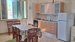 A kitchen with wooden cabinets, a white refrigerator, and a dining table with chairs. - La Serricella Mare vacation home, bright and comfortable just a stone's throw from the sea (Santa Cesarea Terme)