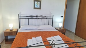 A neatly made bed with an orange bedspread, two bedside lamps, a framed picture on the wall, and a wooden door. - La Serricella Mare vacation home, bright and comfortable just a stone's throw from the sea (Santa Cesarea Terme)