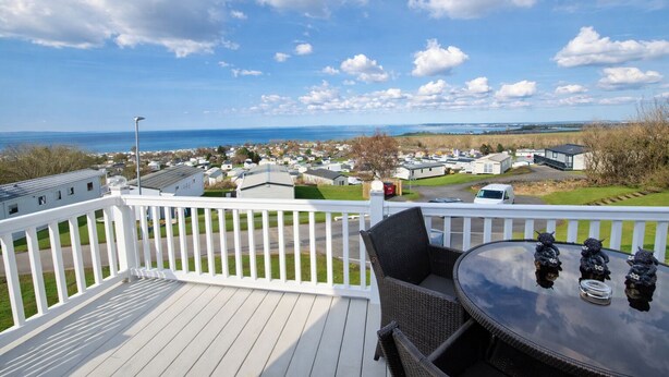 A deck with a table and chairs, overlooking a marina with boats and a distant view of the sea.