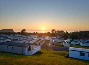 A campground with multiple mobile homes arranged in rows, a clear sky, and the sun setting in the background. - Caravan Sleeps 6 - Sea Views, Parking, Pets (Ayr)