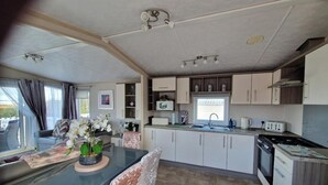 A compact kitchen with a dining area, a window with curtains, and a small refrigerator.