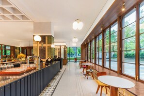 Un espace bar moderne doté d’un long comptoir, de tabourets et de grandes fenêtres offrant une vue sur l’extérieur.