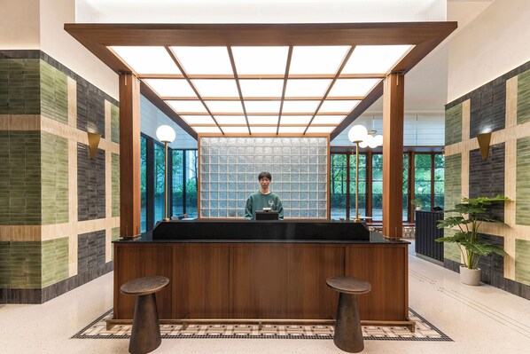 Un comptoir d’accueil avec une personne derrière, une structure de plafond en bois et un mur orné de motifs.