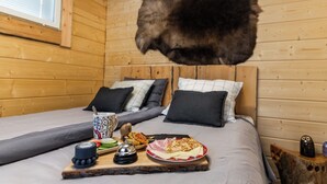 Ein Holzhütten-Zimmer mit zwei Betten, einem Frühstücksbrett und einem Fell, das von der Decke hängt.
