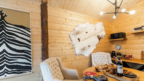 Ein Holzinterieur mit einem gepolsterten Sessel, einem Esstisch mit Flasche und Gläsern, einem aufgehängten Fellstück und einem Kunstwerk mit Zebra-Muster.