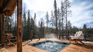 Une terrasse en bois avec un jacuzzi, deux fauteuils à bascule et une vue sur une forêt.