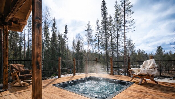 Eine Holzterrasse mit Whirlpool, zwei Schaukelstühlen und Blick auf einen Wald.
